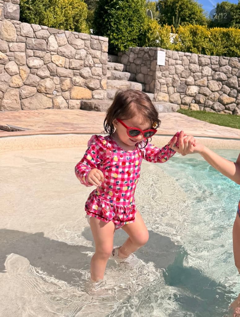 My daughter in red sunglasses holding a hand as she steps through a shallow pool